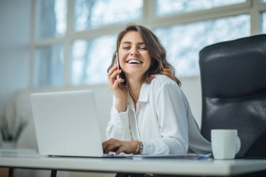 Ofisteki genç kadın cep telefonuyla konuşuyor.