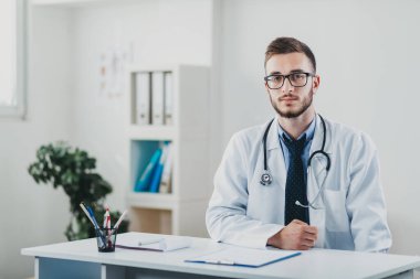 Genç doktor masasının arkasında ofisinde oturuyor.