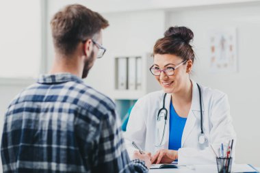 Doktor ve hasta doktorun ofisinde oturuyor.