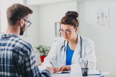 Doktor ve hasta doktorun ofisinde oturuyor.