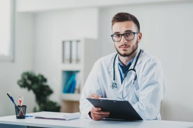 Genç doktor masasının arkasında ofisinde oturuyor.