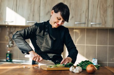 Ahşap bir tahtada çiğ sebze doğrayan kadın şef.