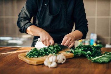 Ahşap bir tahtada çiğ sebze doğrayan kadın şef.