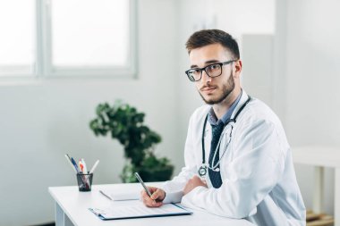 Genç doktor masasının arkasında ofisinde oturuyor.