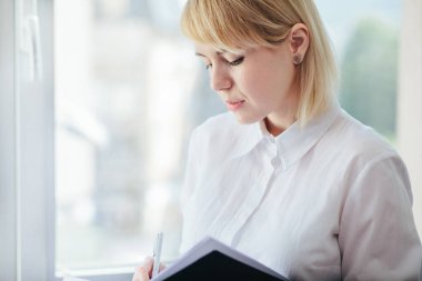 Ofiste çalışan, not defterinde yazan bir kadın.