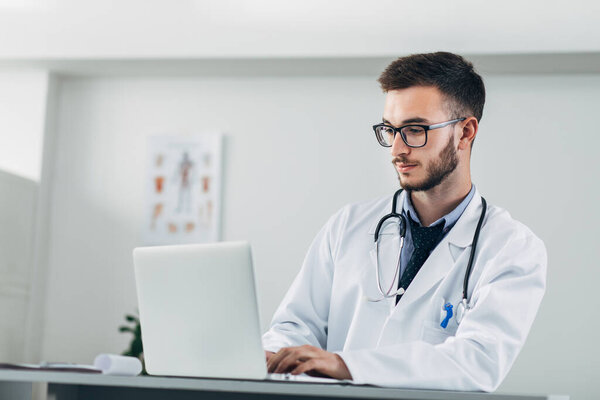 Young doctor working on laptop in his office