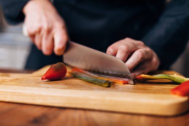 Ahşap bir tahtada kırmızı biber dilimleyen şef.