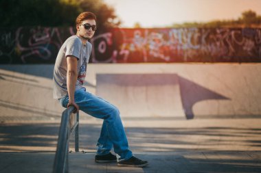 Gün batımında kaykay parkında oturan genç adam.