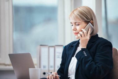 Ofisinde cep telefonuyla konuşan genç bir kadın.