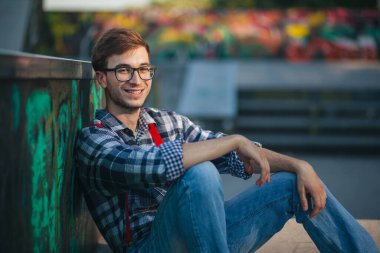 Gün batımında kaykay parkında oturan genç adam.