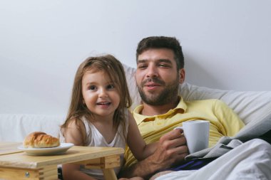 Baba ve kızı sabahları yatakta kahvaltı yapıyorlar. Babam gazete okuyor.