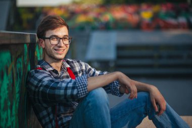 Gün batımında kaykay parkında oturan genç adam.