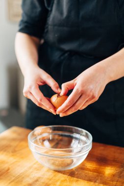 Kadın aşçı cam bir kaseye yumurta kırıyor.