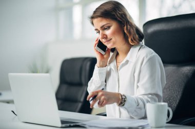 Ofiste çalışan genç bir kadın cep telefonuyla konuşuyor.