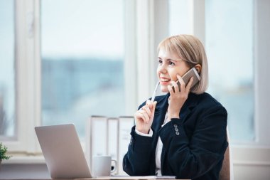 Ofisinde cep telefonuyla konuşan genç bir kadın.
