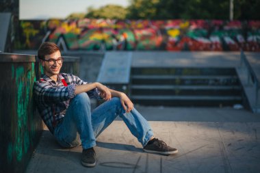 Gün batımında kaykay parkında oturan genç adam.