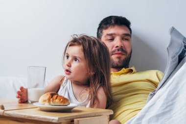 Baba ve kızı sabahları yatakta kahvaltı yapıyor.