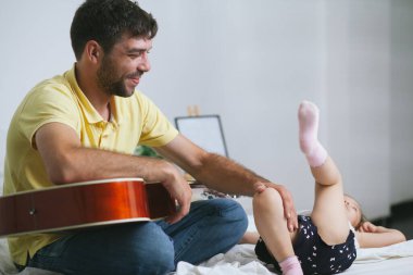 Genç baba, küçük tatlı kızına gitar çalmayı öğretirken onunla eğleniyor.