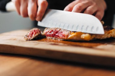 Ahşap bir tahtada pirzola dilimleyen şef.