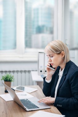 Ofisinde cep telefonuyla konuşan genç bir kadın.