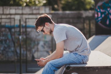 Gün batımında kaykay parkında oturan genç adam.