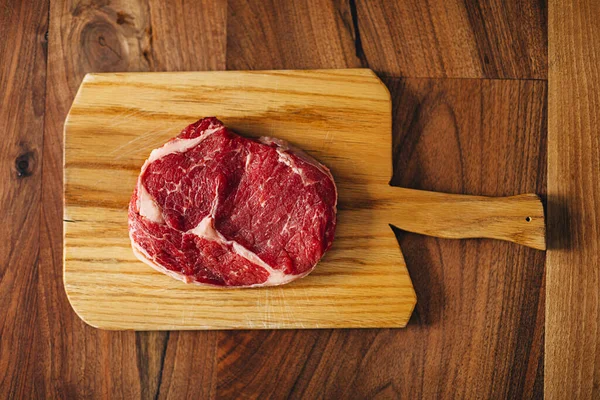 Overhead shot of ribeye steak resting on a wooden board in the kitchen. Top shot