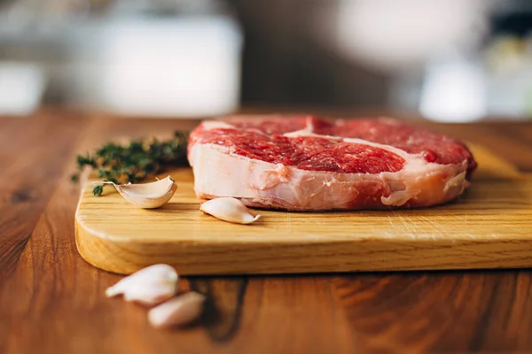 Overhead shot of ribeye steak resting on a wooden board in the kitchen with fresh thyme and garlic cloves. Top shot