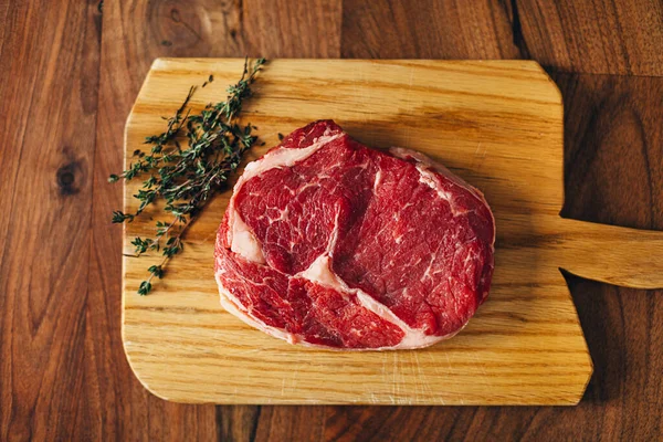 Overhead shot of ribeye steak resting on a wooden board in the kitchen with fresh thyme. Top shot