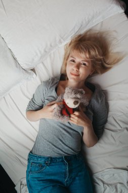 Genç kız peluş ayıyla yatakta yatıyor.