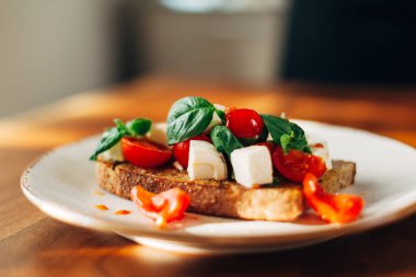 Tost ekmeğinde servis edilen fesleğen ve peynirli vişneli domates.