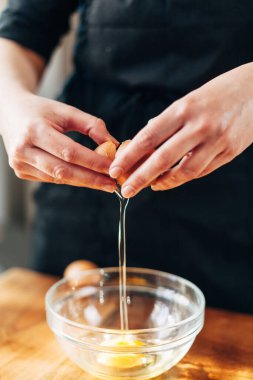 Kadın aşçı cam bir kaseye yumurta kırıyor.