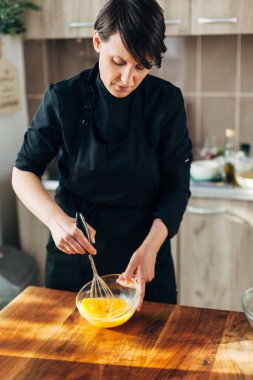 Kadın aşçı cam bir kaseye yumurta atıyor.