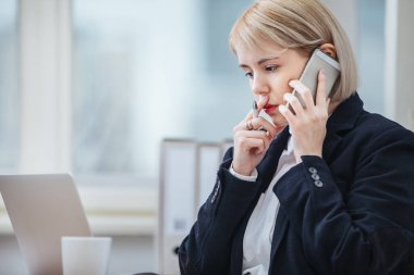 Ofisinde cep telefonuyla konuşan genç bir kadın.