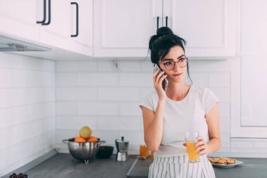 Güzel genç kız mutfakta cep telefonuyla konuşuyor.