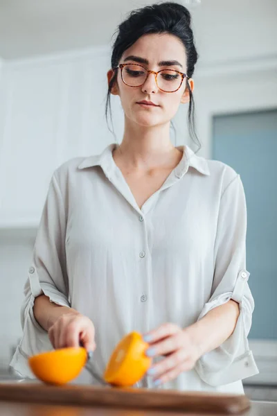 Beautiful young woman cutting orange on the kitchen counter