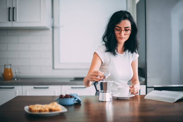 Beautiful young woman pouring coffee in the kitchen