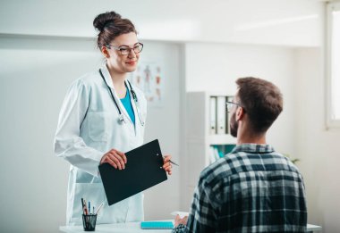 Kadın doktor hastalığını tedavi etmeden önce genç hastaya sonuçları okur.