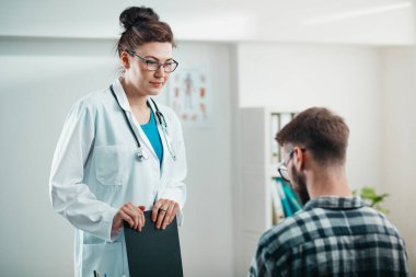 Kadın doktor hastalığını tedavi etmeden önce genç hastaya sonuçları okur.