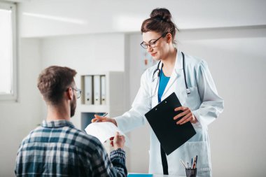 Kadın doktor hastalığını tedavi etmeden önce genç hastaya sonuçları okur.