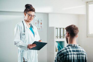 Kadın doktor, hastalığını tedavi etmesi için genç hastaya ilaç yazıyor.