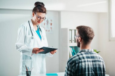 Kadın doktor hastalığını tedavi etmeden önce genç hastaya sonuçları okur.