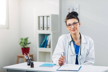Tıp bürosundaki doktor kameraya bakıyor.