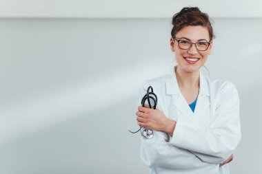 Hastane ofisinde steteskop tutan gülümseyen genç bayan doktor.