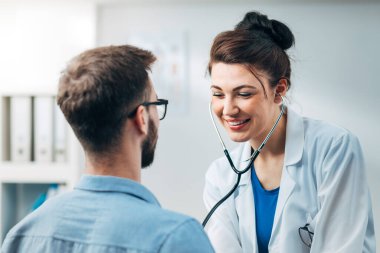 Steteskop kullanan kadın doktor hastanın göğsünü kontrol ediyor.