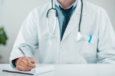 Stetoskop ve yaka kartlı Beyaz Doktor üniformasının ayrıntıları. Erkek doktor elinde kalem tutuyor..
