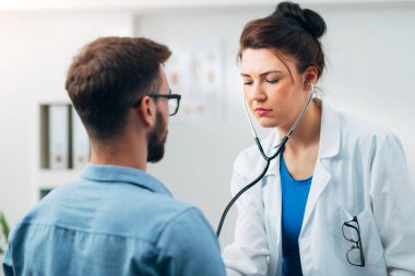 Steteskop kullanan kadın doktor hastanın göğsünü kontrol ediyor.