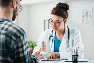 Kadın doktor hastalığını tedavi etmeden önce genç hastaya sonuçları okur.