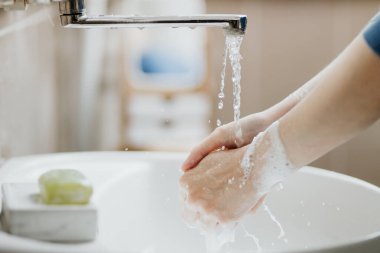 Covid-19 virüsünü önlemek için ellerini banyoda yıkayan bir kadının fotoğrafı. Koronavirüs salgını sırasında sabun ve akan suyla yıkanması tavsiye edilir..
