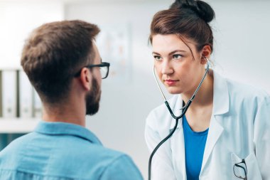 Steteskop kullanan kadın doktor hastanın göğsünü kontrol ediyor.