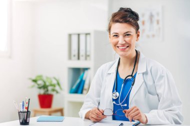 Kadın doktor stetoskopla muayenehanesinde oturuyor.